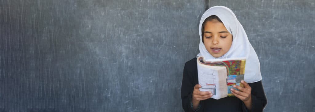 Girl reading in front of blackboard in class